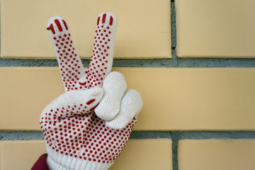 Gesture of victory.Man hand victory sign hand in a construction glove against a yellow brick wall.
