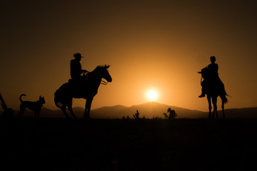 horses, cowboys, dogs at sunset