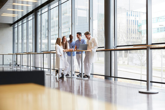 Full length healthcare workers discussing over laptop on table in corridor against window at hospital