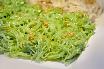 Close-up green egg noodles on the white plate with fried garlic on top