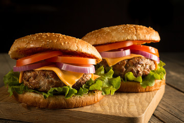 Home made hamburger with beef, onion, tomato, lettuce and cheese. Fresh burger close up on wooden rustic table with potato fries, beer and chips. Cheeseburger.