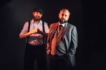 Two bearded men in vintage suits like a gangsters angry looking on the black background