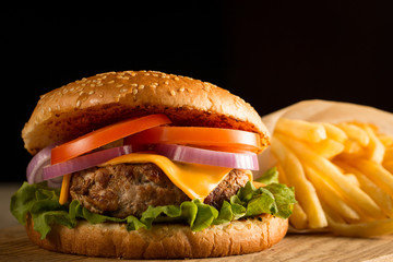 Home made hamburger with beef, onion, tomato, lettuce and cheese. Fresh burger close up on wooden rustic table with potato fries, beer and chips. Cheeseburger.