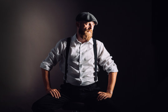 Portrait on a bearded man in white shirt and suspenders on black background in studio