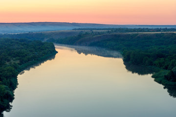 The dark forest on the shore of tranquil river. Foggy early morning. Seversky Donets river, Russia