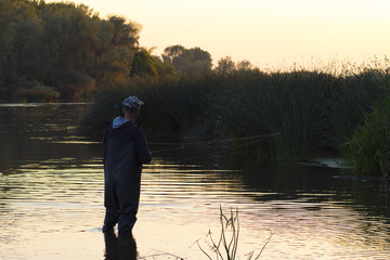 The fisherman stands in the river in the evening and catches fish for spinning