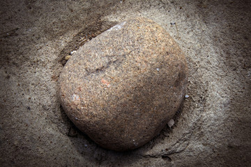 Small round granite stone half fixed in concrete surface, background with darkened vignette