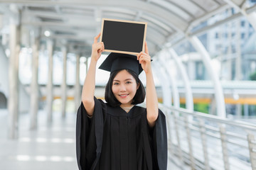 Asian beautiful graduate girl smiling and show blank board in campus , graduation concept