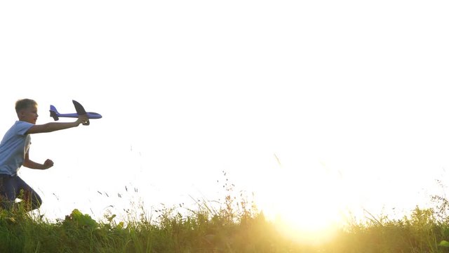 Silhouette of cute 11 years old kid playing toy airplane outside in sunny sunset meadow on summer holidays in countryside. Dreaming about trips, travelling and journeys concept. Real time 4k video.