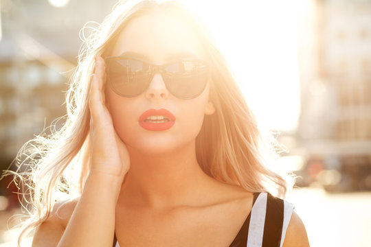 Closeup portrait of glamor blonde girl wearing glasses, walking at the street in sunny evening. Space for text