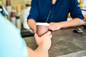 Hand of barista at bar serve coffee for client. Hand gives cup to client visitor. Enjoy your drink. Man receive drink at bar counter. Cappuccino or cacao with straw. Served in paper cup coffee to go