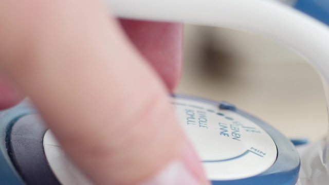 Male Fingers Turning The Temperature Regulator Of Iron.