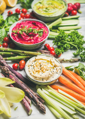 Healthy raw summer vegan snack plate. Chickpea, beetroot, spinach hummus dips with colorful fresh vegetables and greens on white table background. Clean eating, dieting, vegan or vegetarian party food