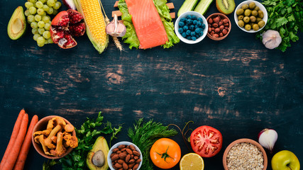 A set of healthy food. Fish, nuts, protein, berries, vegetables and fruits. On a black wooden background. Top view. Free space for text.
