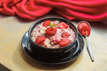 Homemade porridge with strawberries and grains in the black bowl 