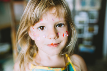 Portrait of adorable little girl with paints on face .