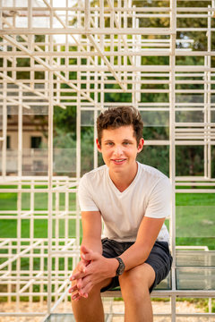 Front portrait of a smiling teenage boy sitting on a abstract art steel frame outdoors.