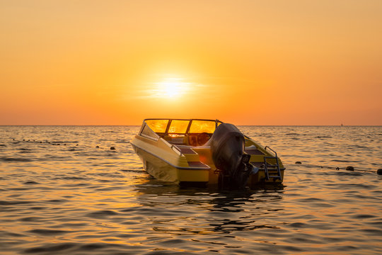 Close beautiful sea view of orange and yellow sunset with a moored motorboat against the horizon.