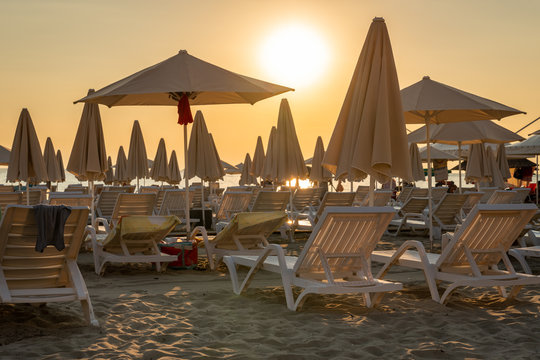 Beautiful yellow sky and many sunchairs, sun umbrellas and parasols on a beach in Albania late afternoon.