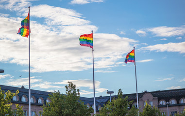 Rainbow flags on flagpoles fluttering in the wind against the blue sky in the city, a symbol of...