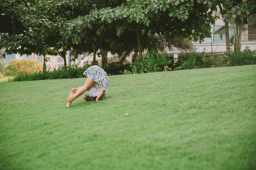 Fototapeta na wymiar Portrait of adorable little girl somersaulting on green grass .