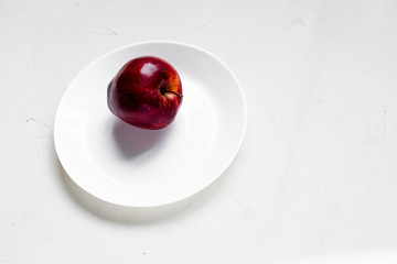 A ripe red apple on a white plate. Top view, copy space