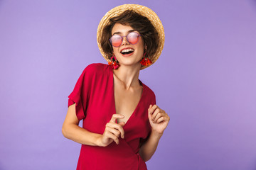 Image of fashionable brunette woman 20s in straw hat and sunglasses smiling, isolated over violet...