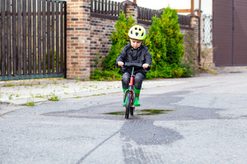 Boy in green helmet ride balance bike (run bike). Childhood