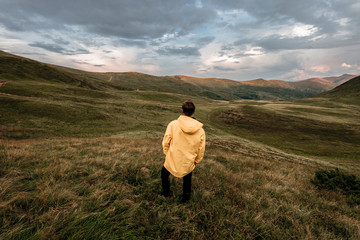 Naklejka na ściany i meble A young guy in a yellow raincoat on top of a mountain. Carpathians, Ukraine