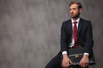 seated young businessman holds suitcase and looks to side