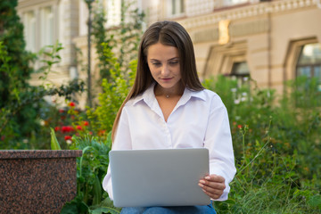 Young beautiful female with a laptop sits on a bench in a city.