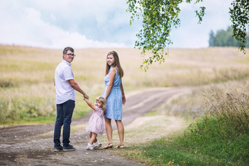 Naklejka na ściany i meble Family mother, father and little daughter beautiful and happy outdoors on the road in the field