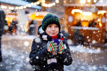 Little cute kid boy drinking hot children punch or chocolate on German Christmas market. Happy...