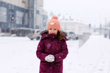 Adorable little kid girl in colorful clothes playing outdoors during snowfall