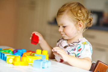 Adorable toddler girl playing with educational toys in nursery. Happy healthy child having fun with colorful different plastic blocks at home. Cute baby learning creating and building.