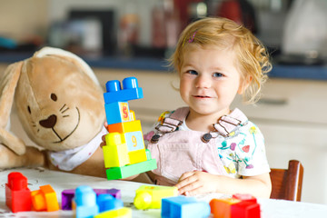 Adorable toddler girl with favorite plush bunny playing with educational toys in nursery. Happy...