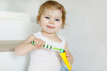 Little baby girl holding toothbrush and brushing first teeth. Toddler learning to clean milk tooth.