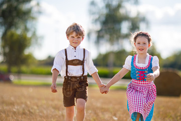 Two kids, boy and girl in traditional Bavarian costumes in wheat field with hay bales