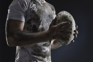 Rugby player hands with ball on dark background. Close up