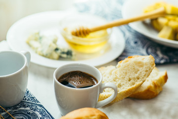  couple of cups with coffee, cheese, honey, baguette and fruit on a light marble table