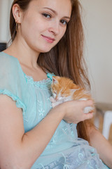 Close up of cute kitten in woman's hands. Pretty woman holding a cat closely to the camera. Indoor. Adorable kitty