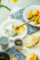  couple of cups with coffee, cheese, honey, baguette and fruit on a light marble table