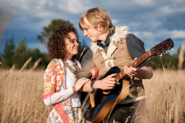 Boho style attractive couple in love posing on the autumn field. Family having fun and laughing, play guitar. Gypsy style clothes. Young blonde man and beautiful caucasian woman together outdoor.