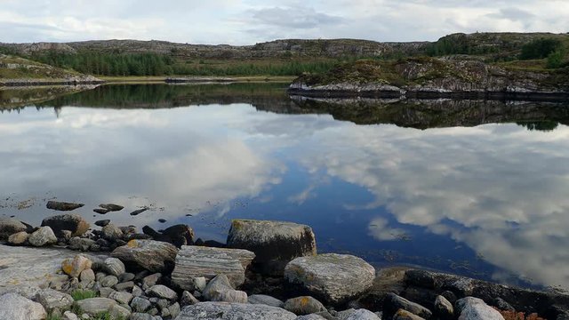 Rocks and clouds are reflected in the water Norwegian fjord in sunny day, Averoy, Norway

