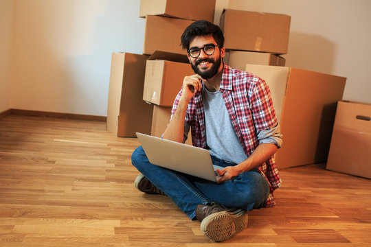 Young man moving into a new house.He sitting on floor in empty apartment and calculate home budget.