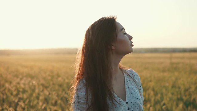 Close-up shot of a wonderful brunette girl spending time in countryside, fantastic open meadow. Young girl enjoying warmth of the sun in the evening, sun going down.