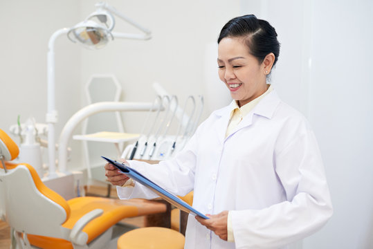 Adult Asian Woman In Dental Office Holding Clipboard And Reading Paper With Smile Working In Clinic