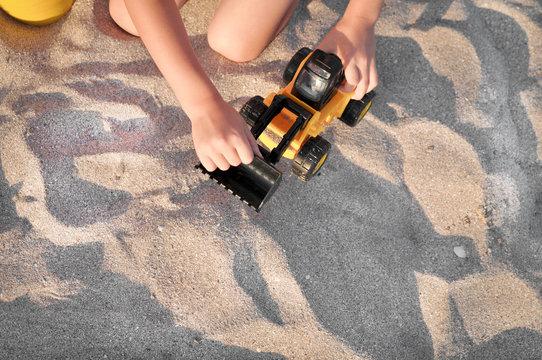 Child playing with a toy tractor on the beach.