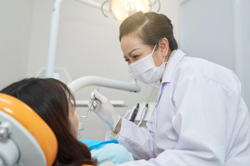 Obraz na płótnie Canvas Professional adult Asian woman in mask and gloves working with anonymous woman in dental chair