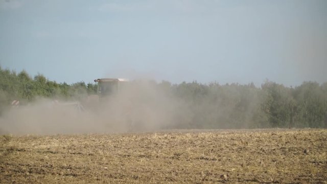 Traktor zieht Pflug durch trockenes Feld in Staubwolke, Waldrand im Hintergrund